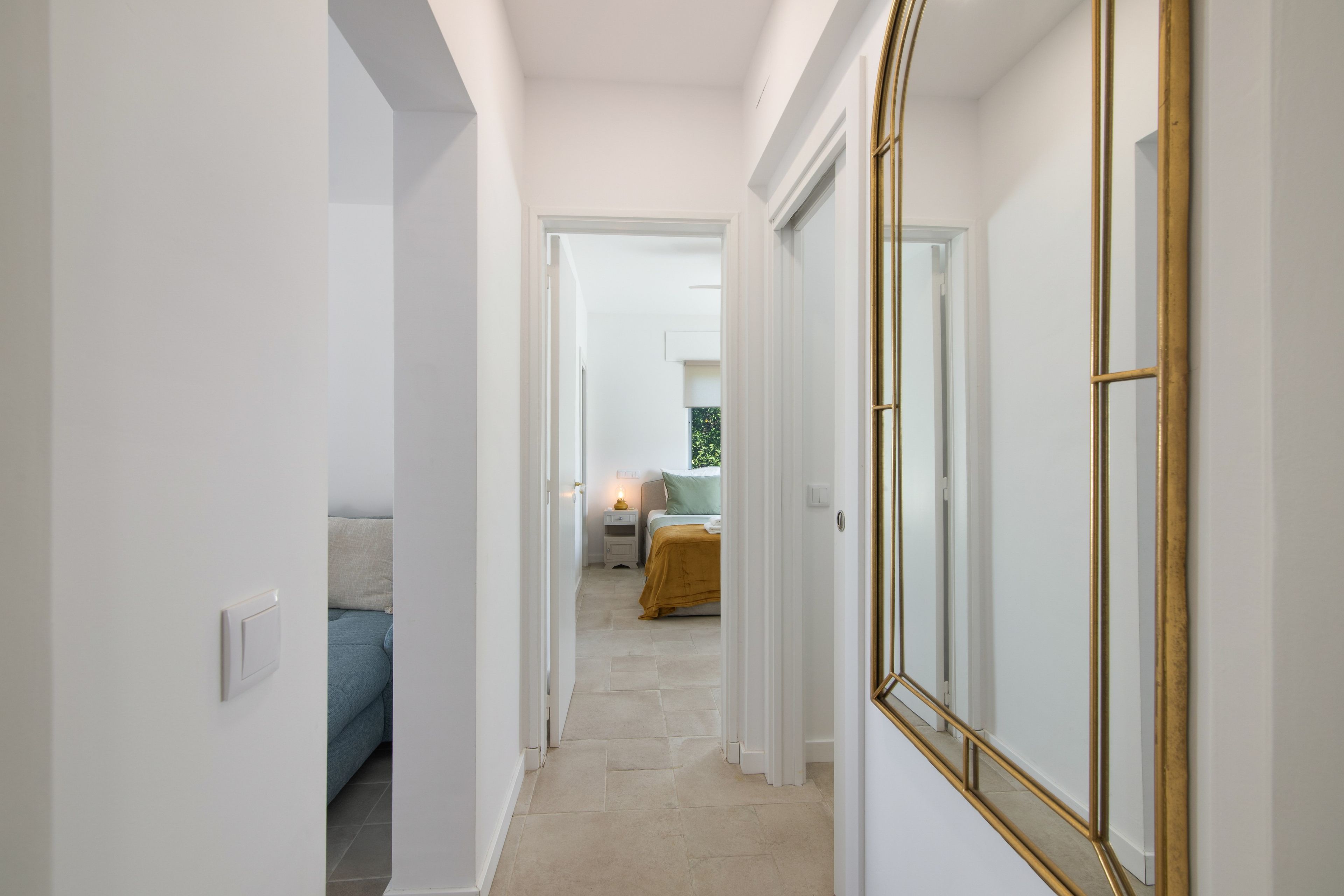 A hallway leading to a bedroom with a bed, bedside table, and a mirror.
