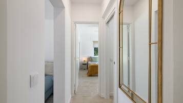 A hallway leading to a bedroom with a bed, bedside table, and a mirror.