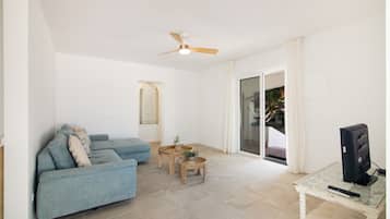 A living room with a sofa, a coffee table, a television, and a ceiling fan.