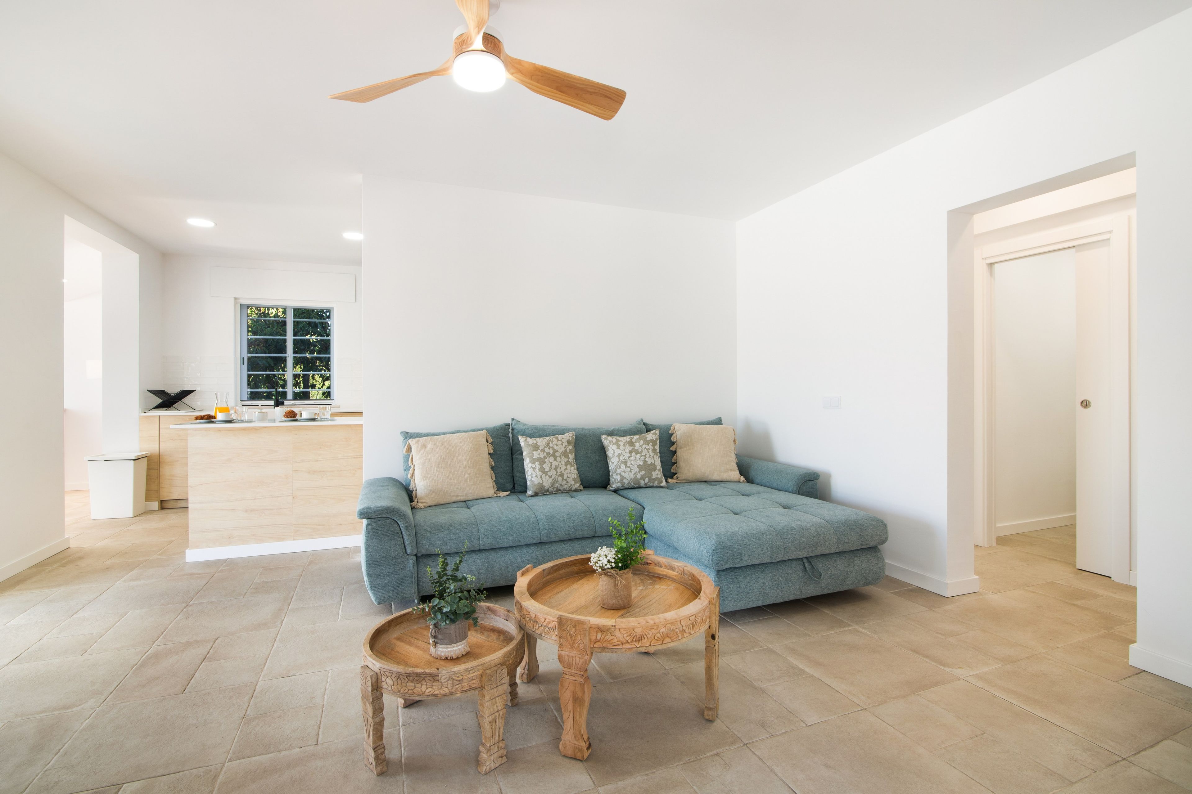 A spacious living room with a blue sofa, two wooden side tables, and a ceiling fan.