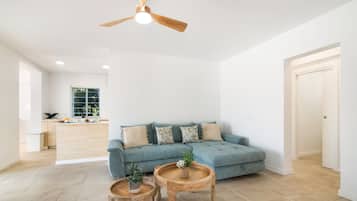 A spacious living room with a blue sofa, two wooden side tables, and a ceiling fan.