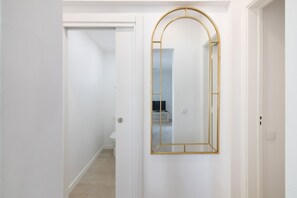 Ein Korridor mit einer weißen Tür und einem spiegel mit goldener Rahmung.