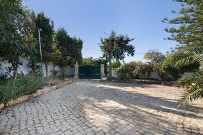 Ein gepflasterter Innenhof mit einer Steinmauer, einem grünen Tor und umgebender Bepflanzung.