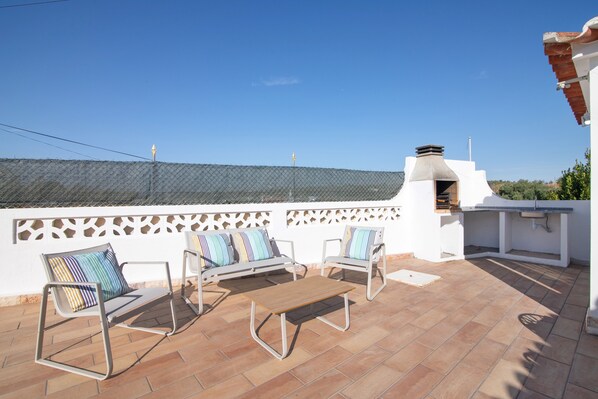 Eine Terrasse mit einer weißen Mauer, einem Metallzaun und Blick zum Himmel.