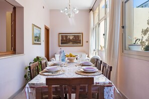 Ein Essbereich mit einem für vier Personen gedeckten Tisch, umgeben von Stühlen, einer Kristallleuchtre und gerahmten Kunstwerken an den Wänden.
