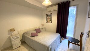 Ein Schlafzimmer mit Bett, Nachttisch, Sessel, Fenster mit Vorhängen und einem Bild an der Wand.