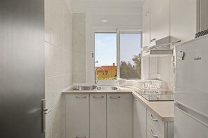 Eine moderne Küche mit weißen Schränken, einer Edelstahl-Spüle und einem Fenster mit Blick auf eine Wohngegend.