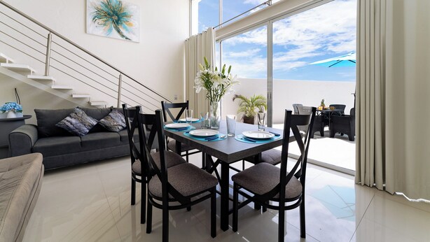 A modern dining area with a table set for four, a staircase, and a large window with a view. - 2BR Main Level | Private Pool Near Beach (Huatulco)