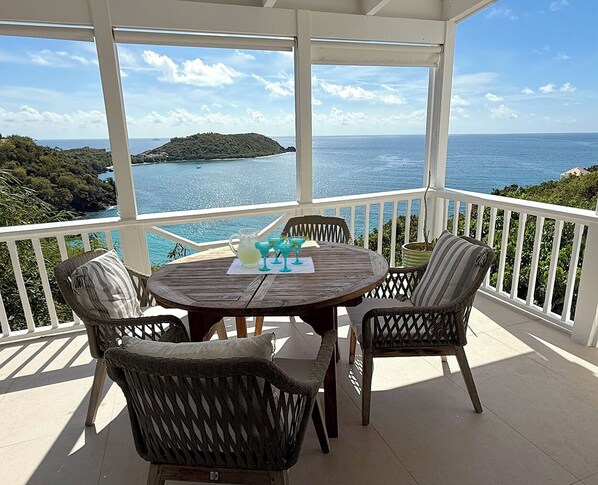A covered outdoor seating area with wicker chairs and a table, overlooking a body of water and a distant island. - Discover Orchid Villa - Your Dream Getaway! Featuring air conditioning throughout for your comfort, and a private pool to relax in. Experience the perfect blend of luxury and convenience! (St John)
