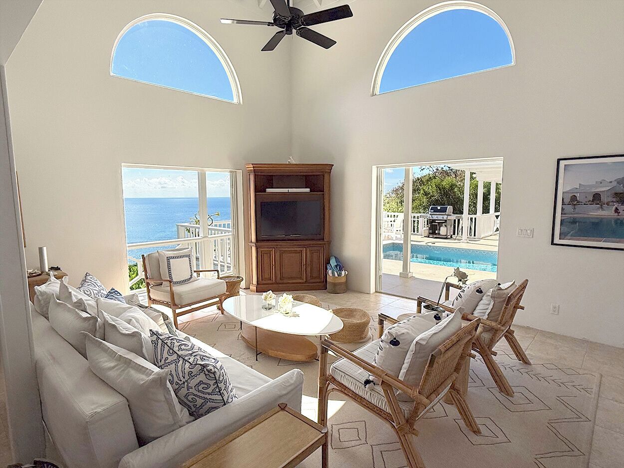 Amplia sala de estar con un ventanal que da a una piscina y al mar, amoblada con un sofá, sillones y una mesa de centro.