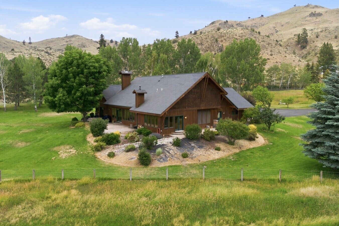 A large wooden house with a sloped roof, surrounded by a well-maintained lawn and a fenced property.