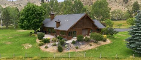 A large wooden house with a sloped roof, surrounded by a well-maintained lawn and a fenced property.