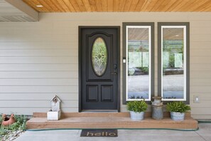 A dark front door with a decorative glass panel, a welcome mat, and two potted plants on the porch. - Private Hot Tub with Perfect Mountain Views (Stevensville)