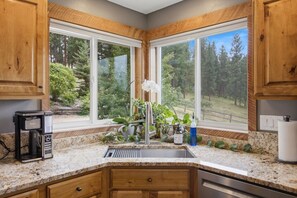 A kitchen with granite countertops, wooden cabinets, a built-in dishwasher, and a window with a view of a forest. - Private Hot Tub with Perfect Mountain Views (Stevensville)