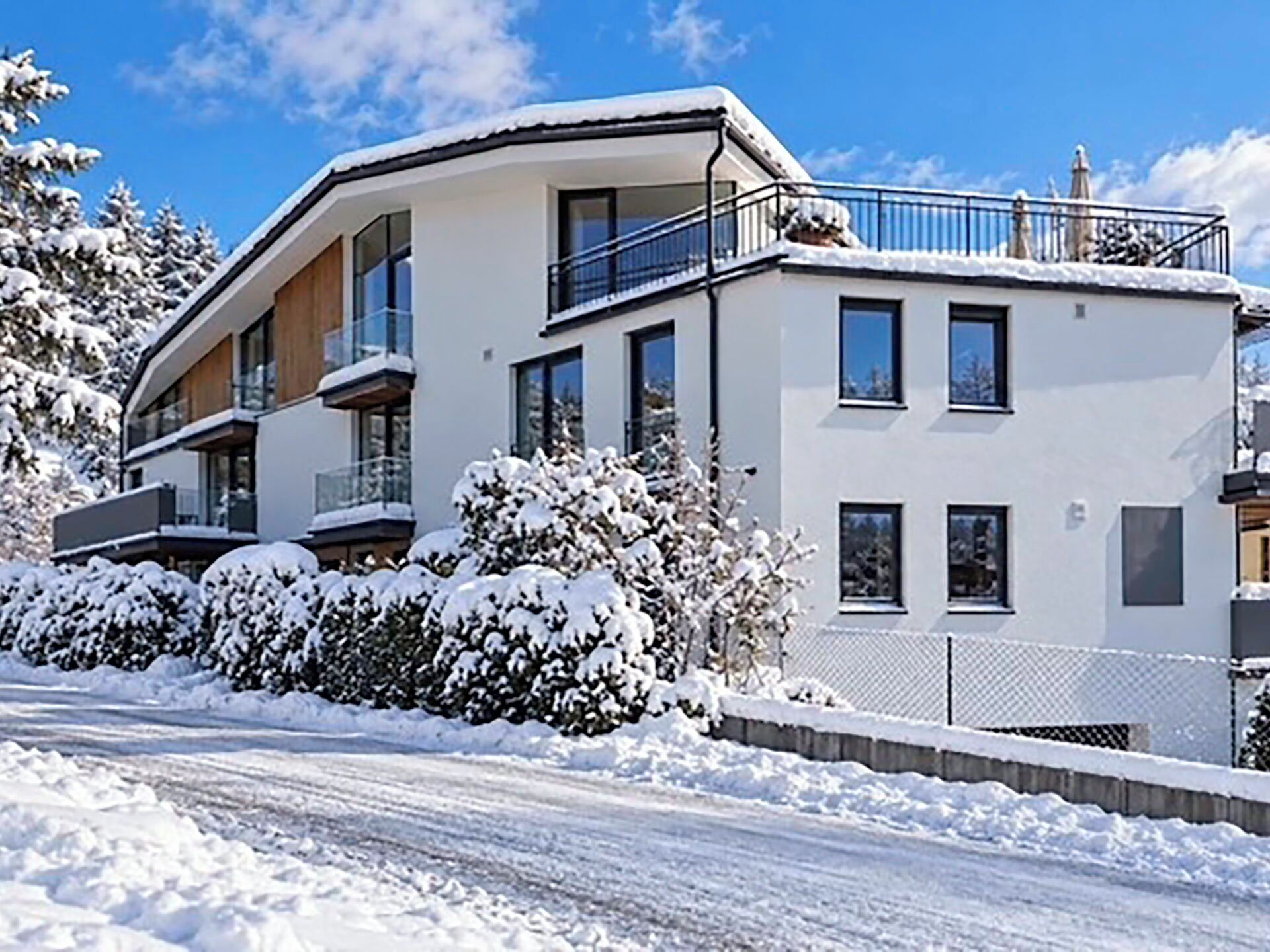 A modern two-story building with a balcony, surrounded by snow-covered trees and bushes.