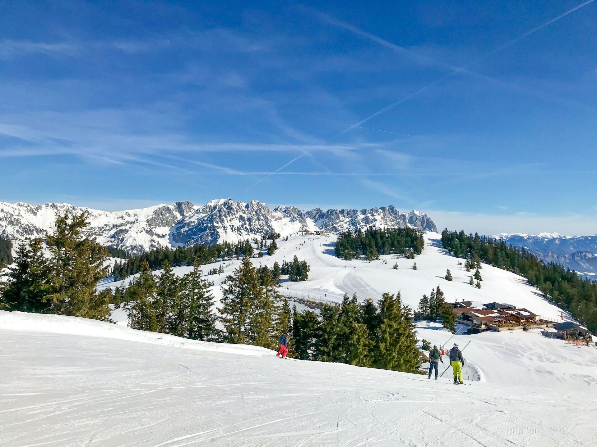 A snowy mountain landscape with ski slopes, a ski lodge, and a clear blue sky.