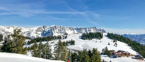 A snowy mountain landscape with ski slopes, a ski lodge, and a clear blue sky.