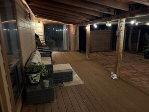 Un espace extérieur abrité doté d’un plancher en bois, d’un coin salon avec des coussins et d’une plante en pot.