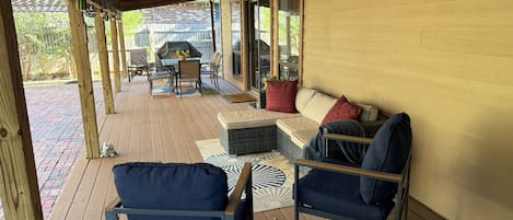Eine überdachte Terrasse im Freien mit Holzdeck, einer Sitzecke mit einer Couch und Stühlen sowie einem Grill.