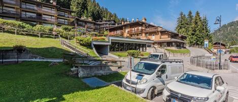 Un hotel con varias edificaciones, una zona de estacionamiento con múltiples autos y un paisaje montañoso de fondo.