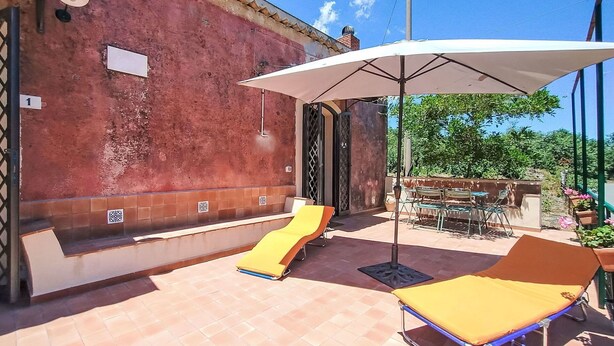Un patio con dos tumbonas, una zona de estar cubierta y suelo de baldosas.
