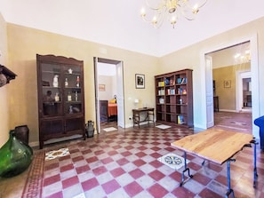Ein geräumiges Wohnzimmer mit Schachbrettmuster-Boden, einem Holztisch, einem Bücherregal und einer Chandelier.