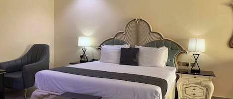 A hotel room with a large bed, two bedside tables with lamps, a chair, and a small table with a remote control.