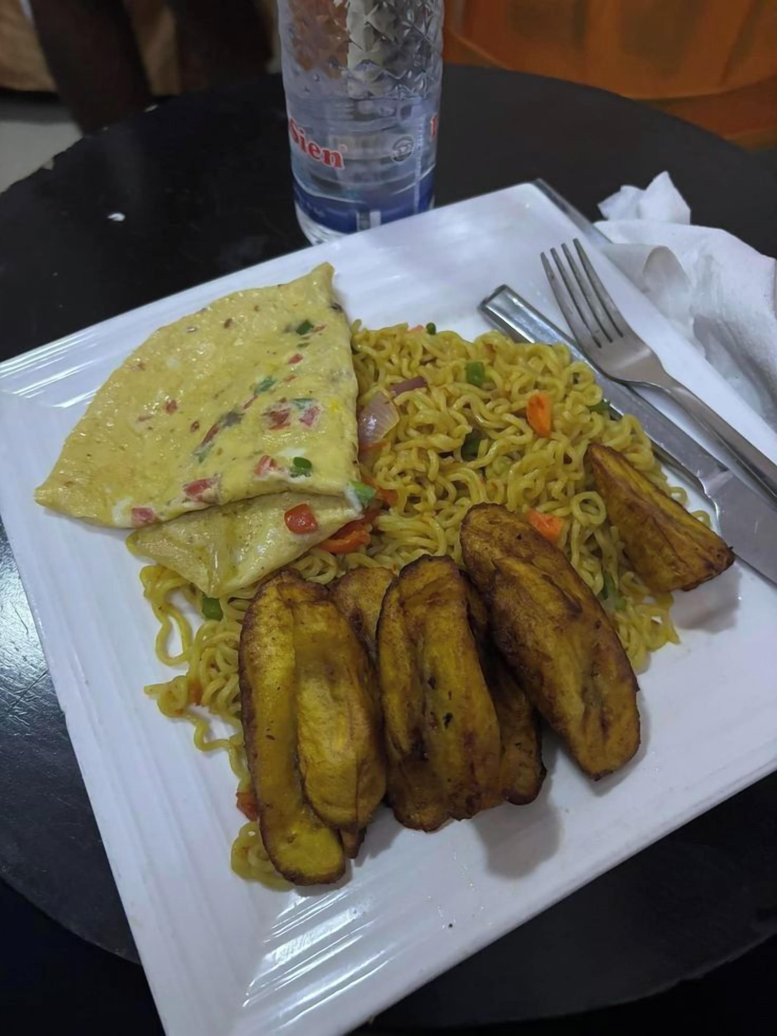 A plate of food with noodles, a fried egg, and fried plantains on a white plate.
