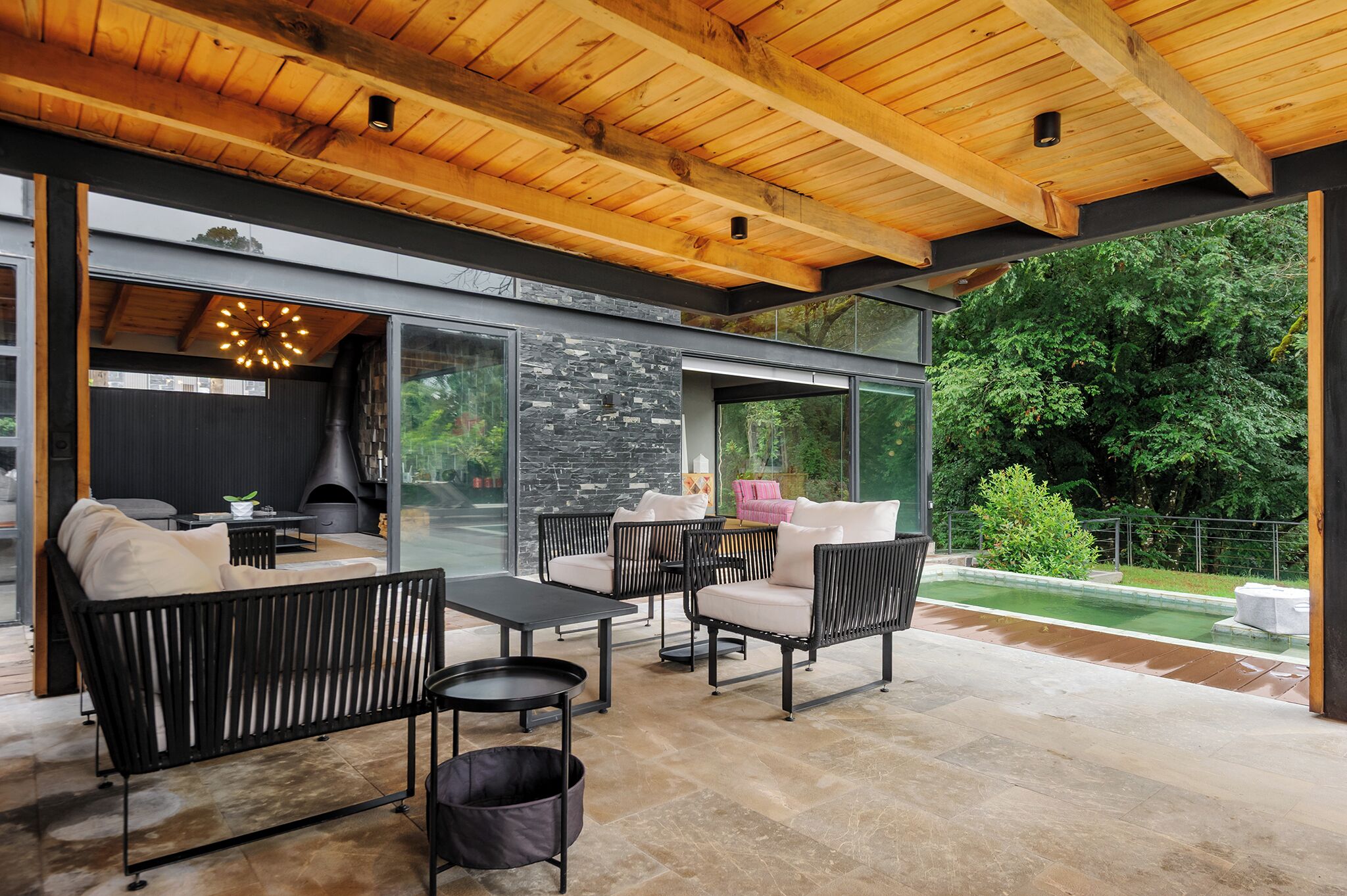 An outdoor seating area with modern furniture, a stone wall, and a view of a garden.