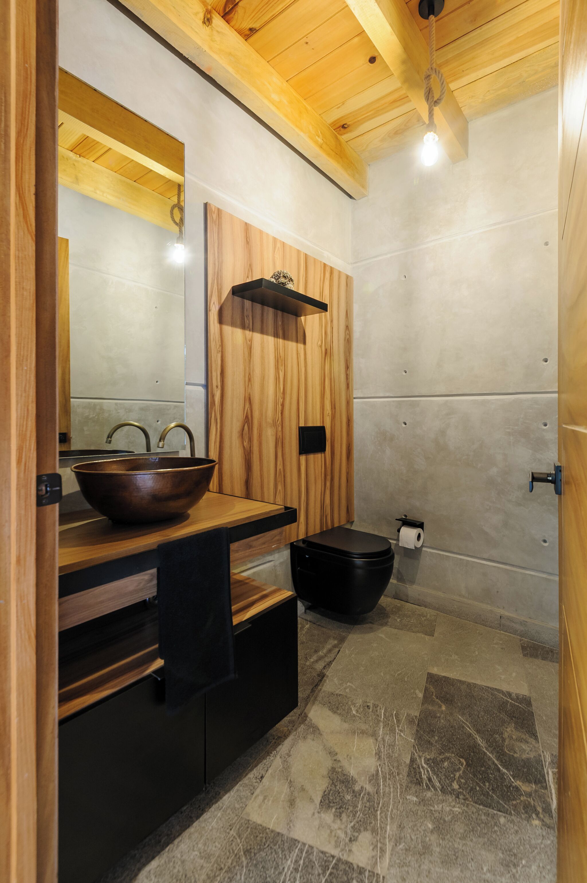 Ein modernes Badezimmer mit einem Holzlagerfeld, einem großen Spiegel, einer schwarzen Toilette und einem Boden aus Steinplatten.