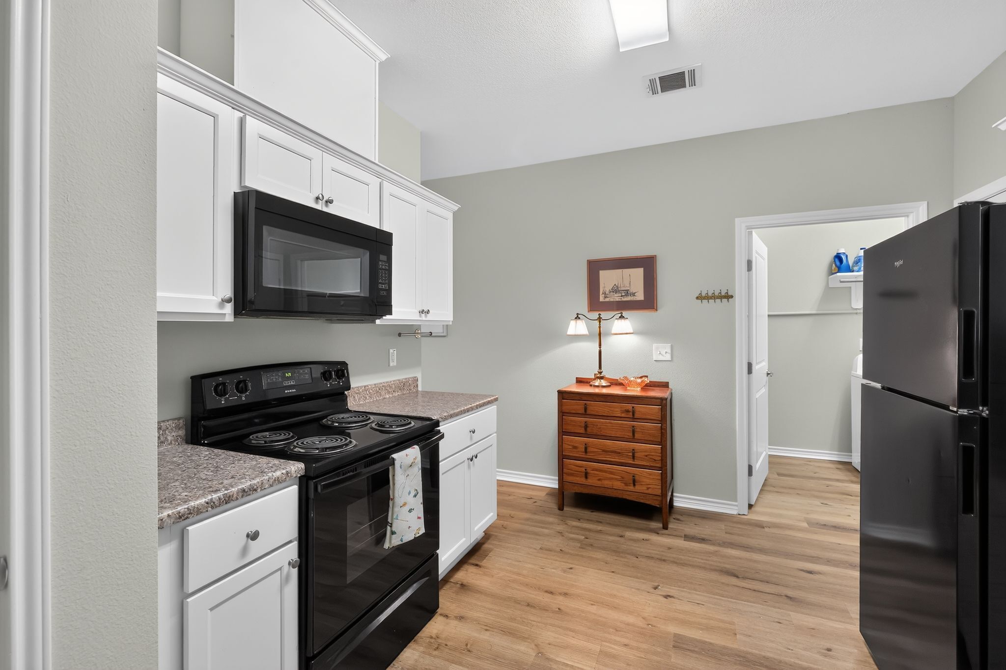 A compact kitchen with white cabinetry, a black stove, a microwave, and a refrigerator.