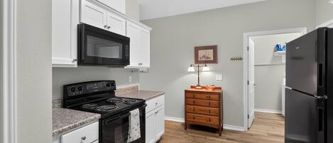 A compact kitchen with white cabinetry, a black stove, a microwave, and a refrigerator.