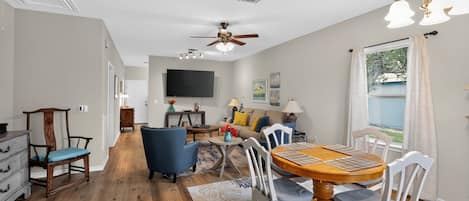 A spacious living area with a dining table, chairs, a ceiling fan, and a television.