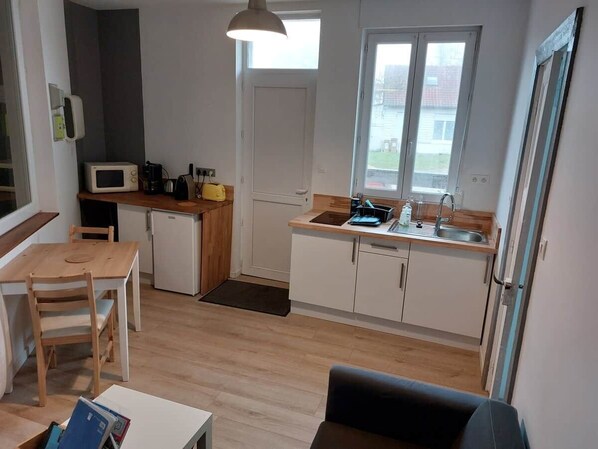 A compact kitchen with a microwave, sink, and wooden dining table. - Vacation Rental in the Somme Bay Area for 2 People (Fort-Mahon-Plage)