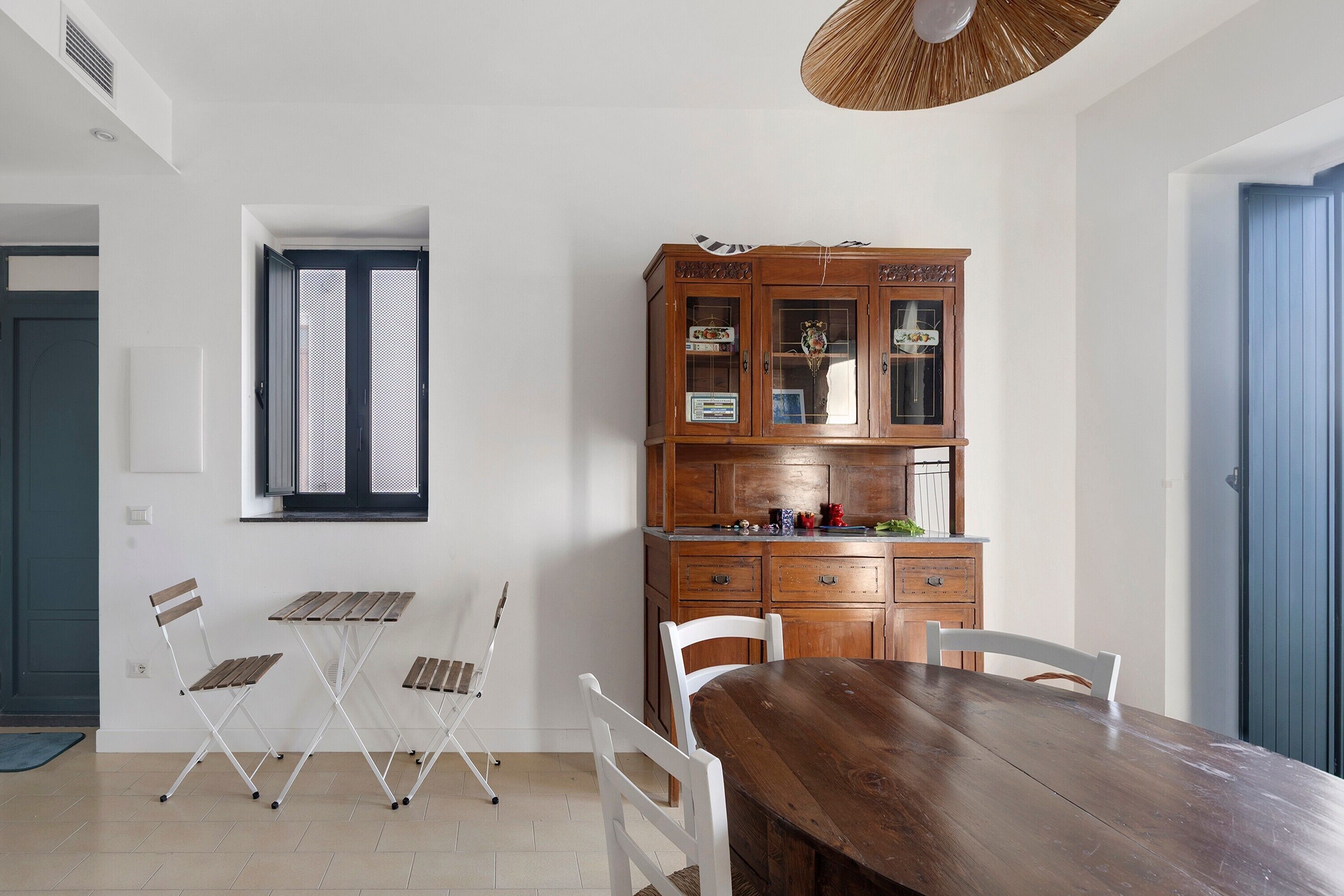 Un coin repas avec une table et des chaises en bois, un meuble avec des portes en verre et une fenêtre avec des volets.