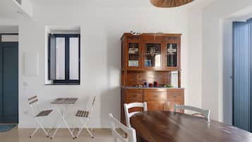 Un coin repas avec une table et des chaises en bois, un meuble avec des portes en verre et une fenêtre avec des volets.