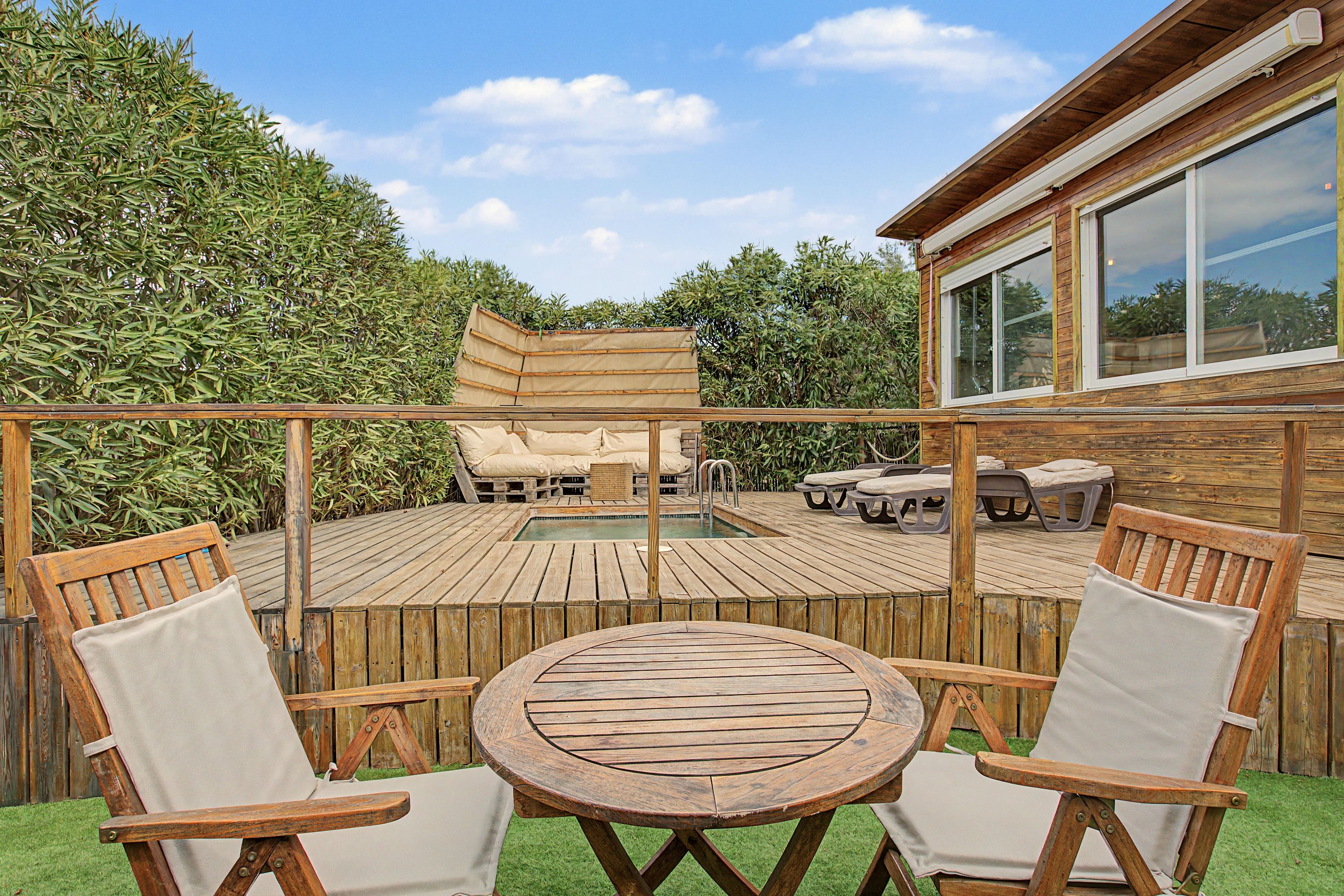 Une terrasse en bois avec une piscine, entourée d’une clôture en bois et d’une haie.