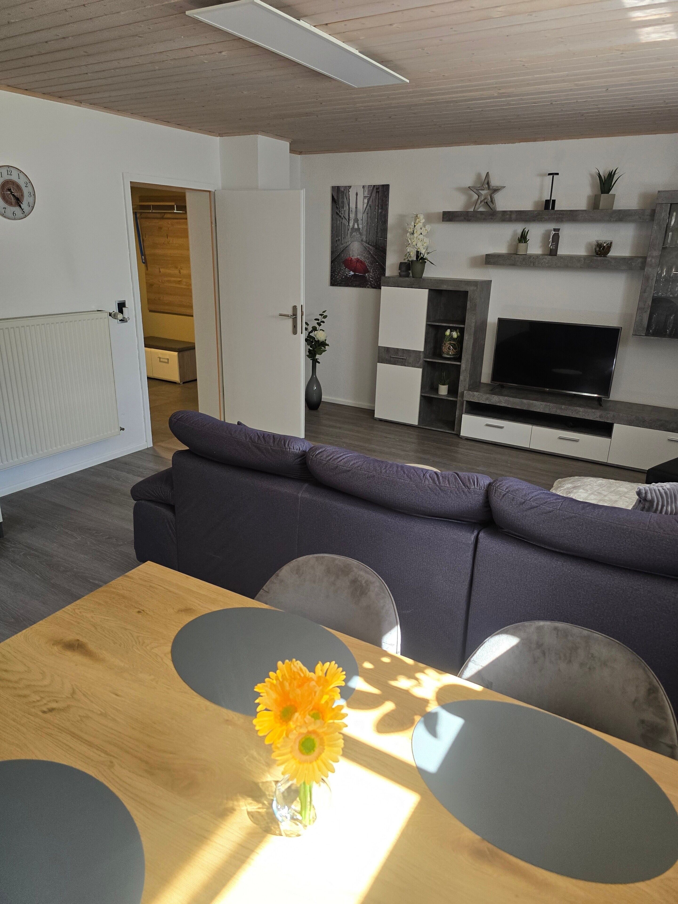 A modern living room with a sofa, a dining table with a vase of flowers, a television, and a fireplace.