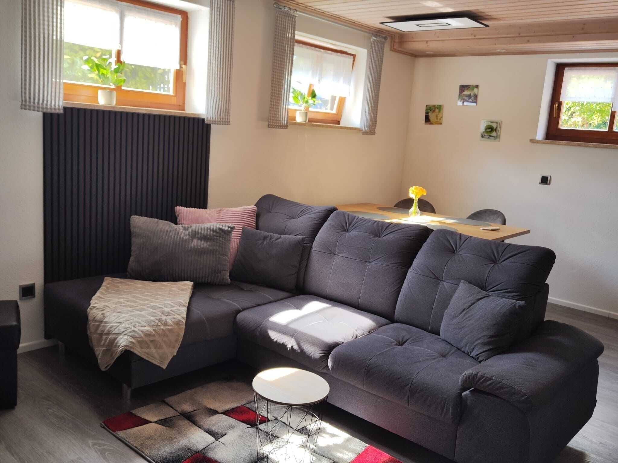 A modern living room with a sectional sofa, a small round table, and a view of the outdoors through windows.