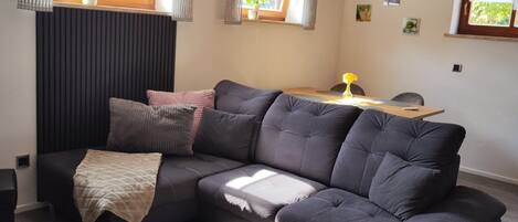 A modern living room with a sectional sofa, a small round table, and a view of the outdoors through windows.