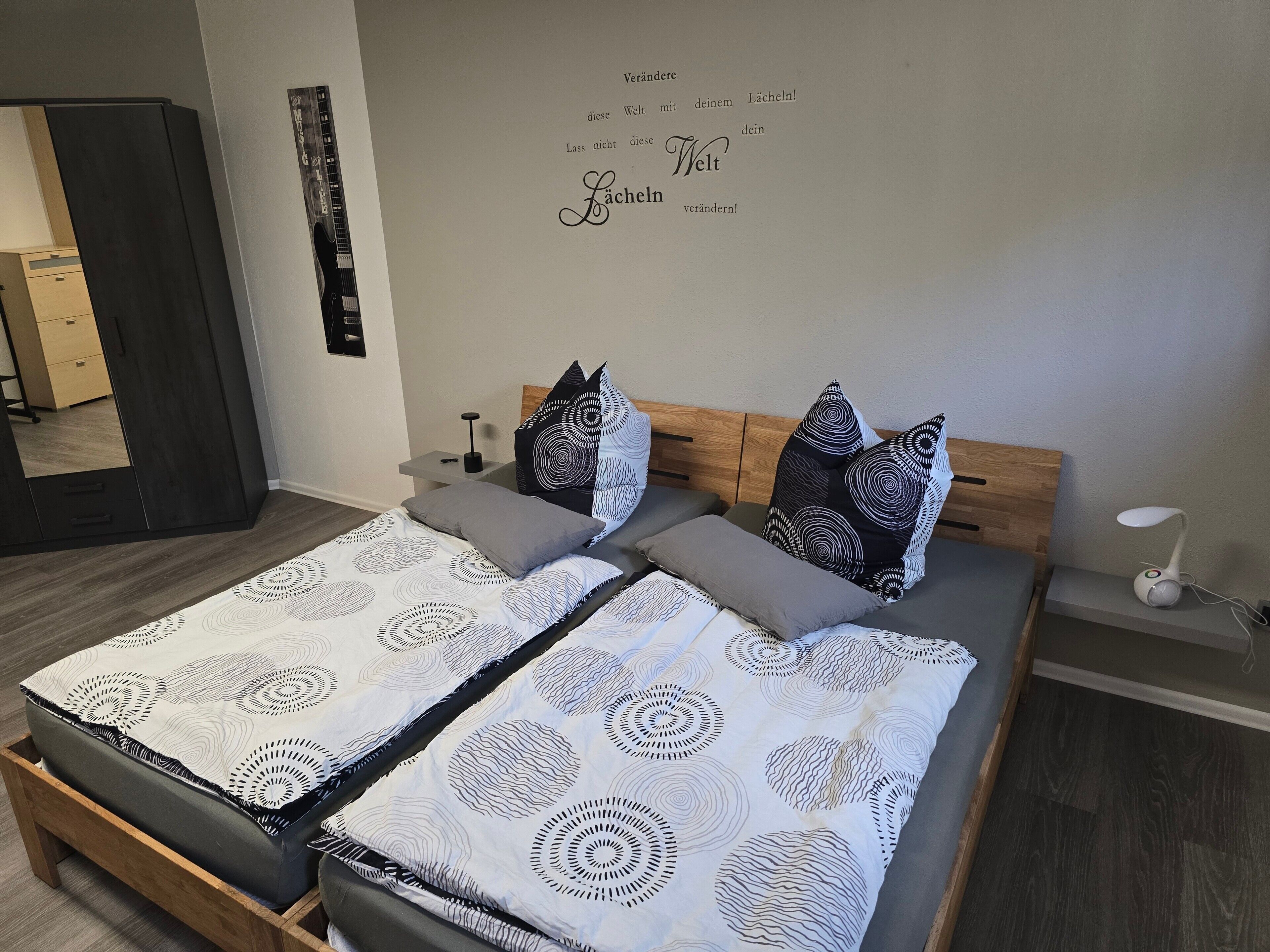 A bedroom with two beds, a mirror, a bedside table, and a wall with text.