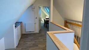 A narrow, sloped hallway with a wooden floor, a white radiator, and a ceiling light. - Ostfriesenfischer (Leezdorf)