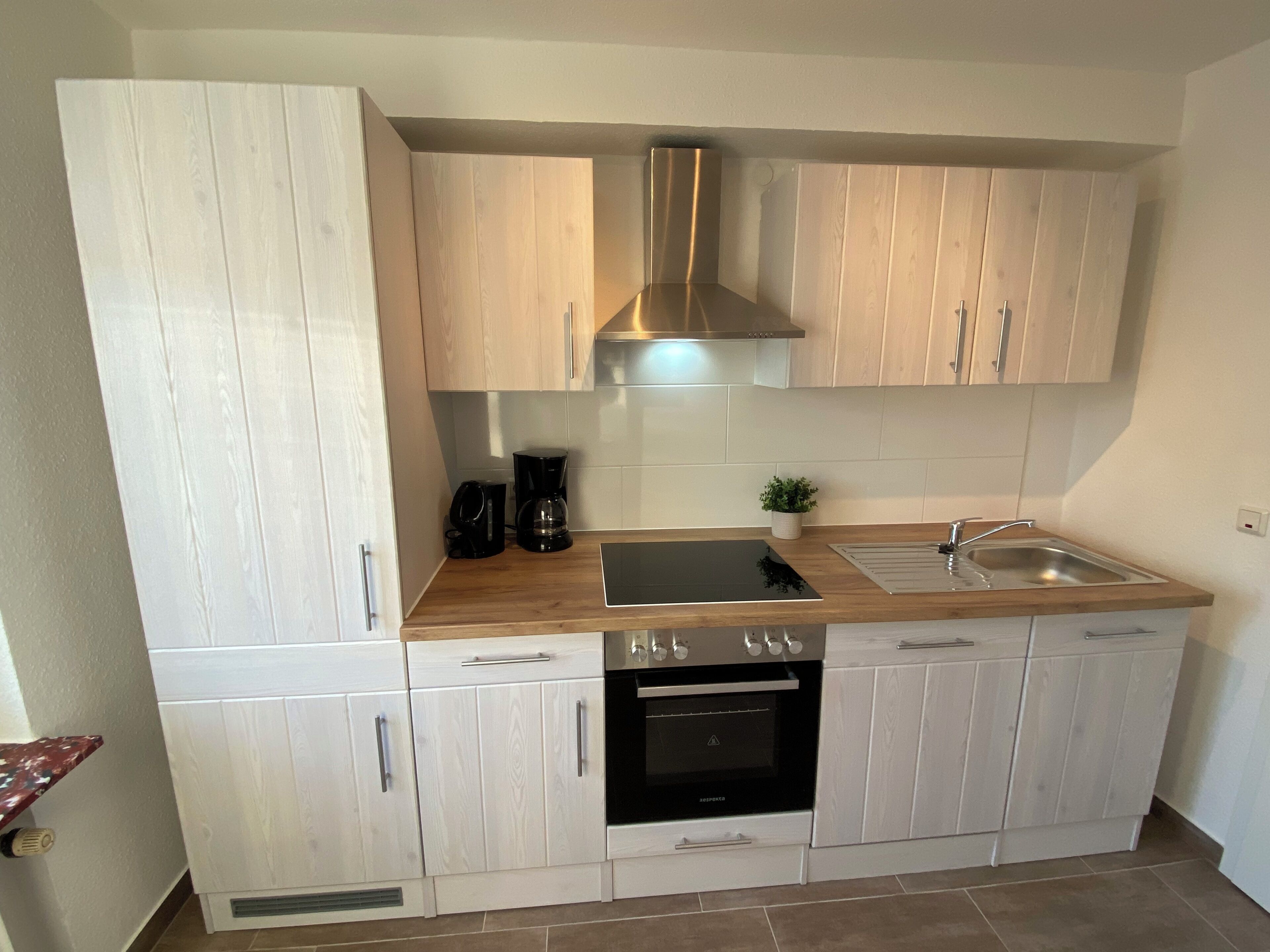 A compact kitchen with white cabinetry, a black stove, a coffee maker, and a small potted plant.