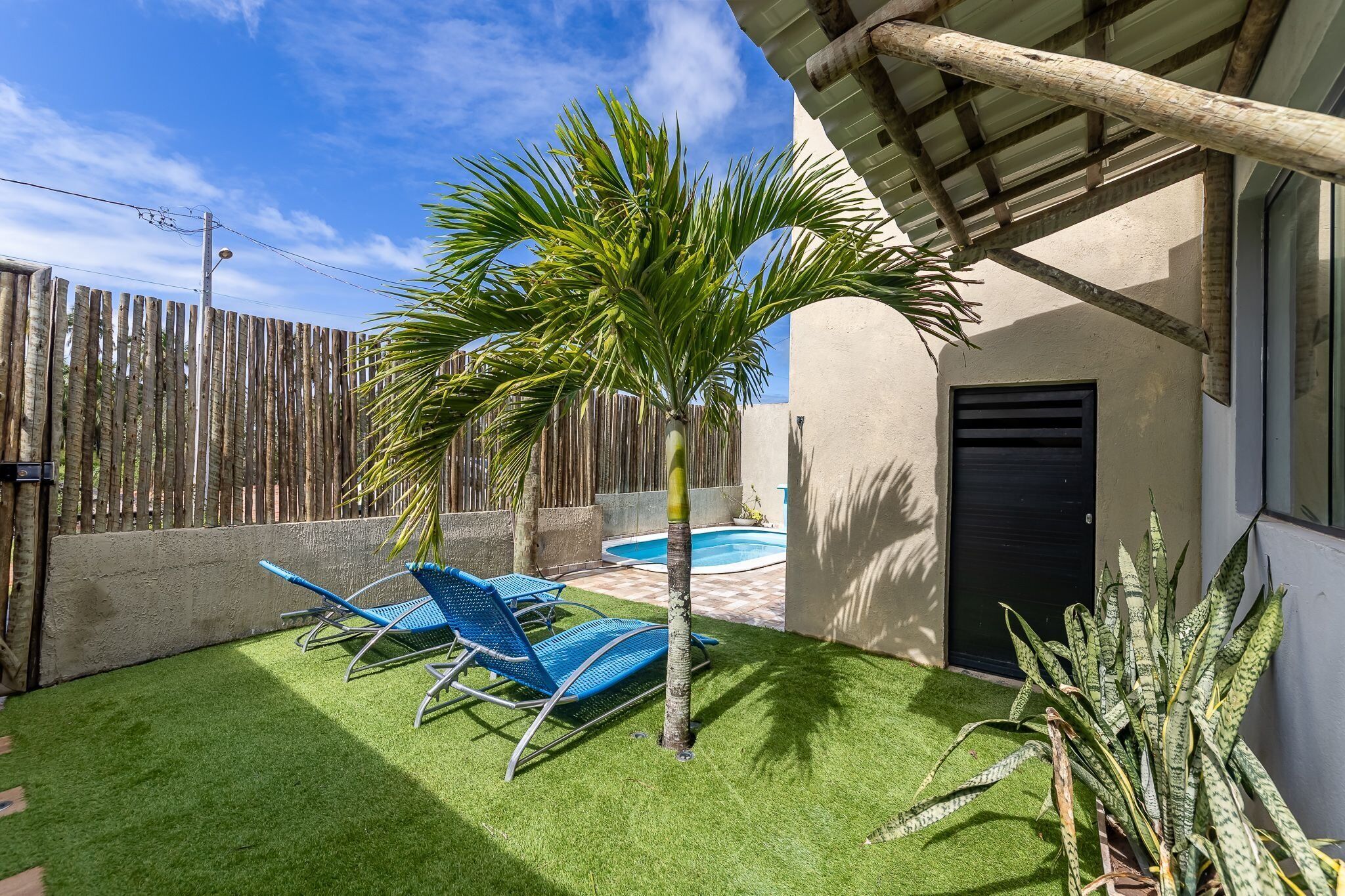 A backyard with artificial grass, a pool, and blue lounge chairs.