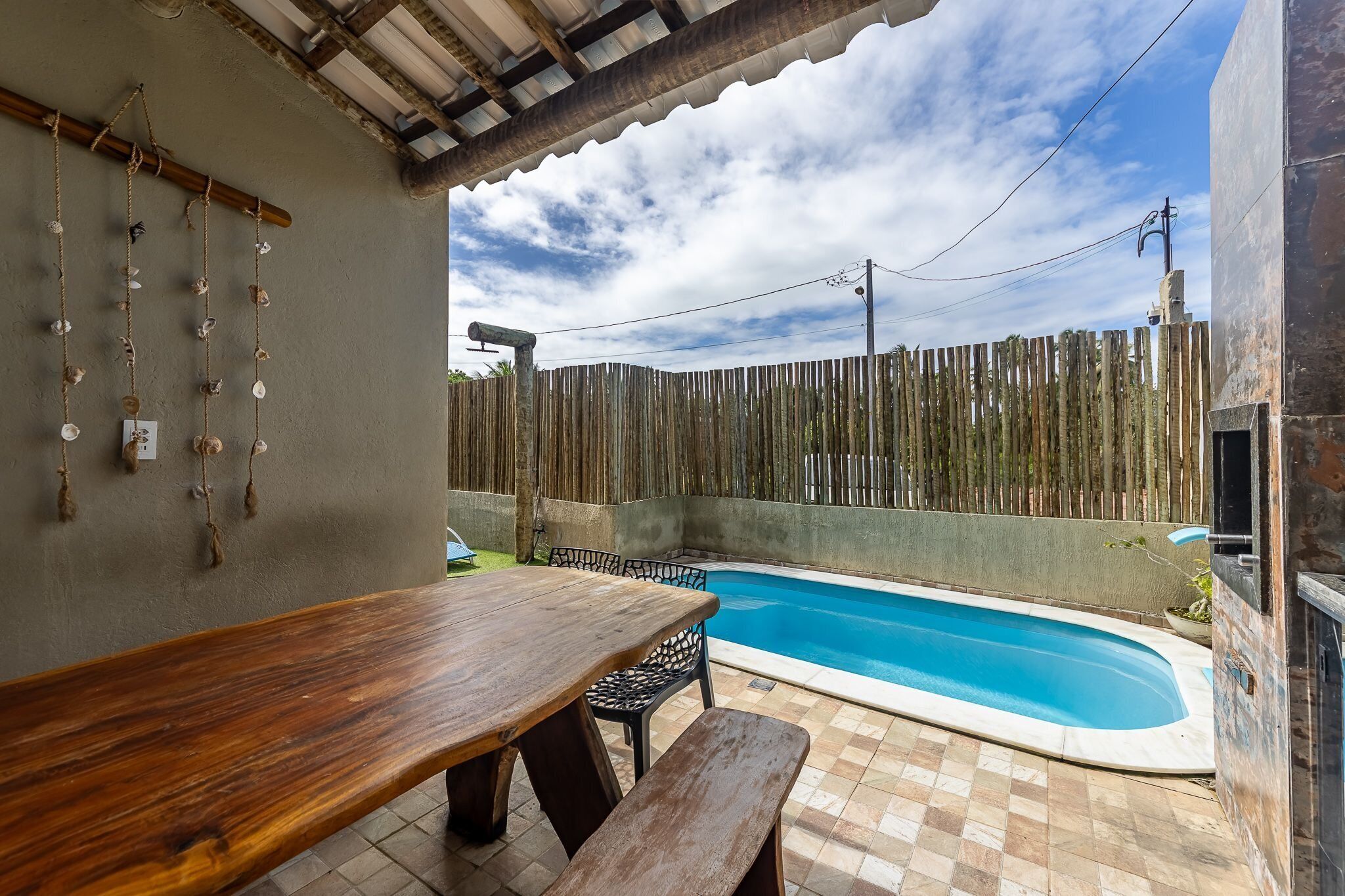 An outdoor patio with a wooden table and chairs, a swimming pool, and a wooden fence.