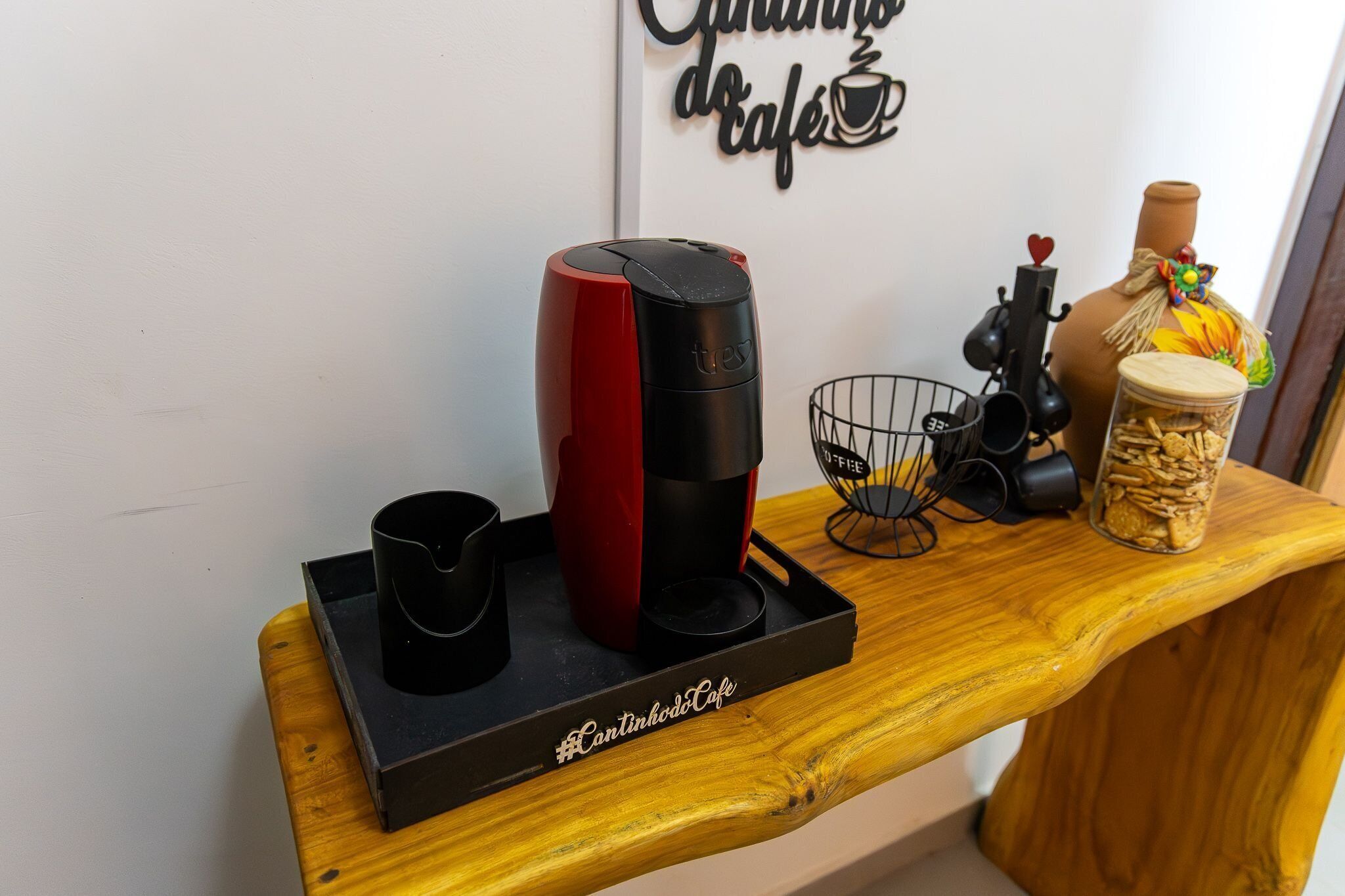 En kaffemaskine, en kop, en kurv, et glas og et skilt på en træbordplade.