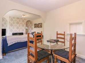 Una habitación con una mesa de vidrio rodeada de sillas de madera, una cama con cubrecama azul y una pared con un cuadro floral.