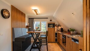 Et moderne køkken med træskabe, et spiseområde med bænk og et stort vindue der giver naturligt lys.
