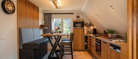 Een moderne keuken met houten kastjes, een zithoek met een bank en een groot raam dat voor natuurlijk licht zorgt.