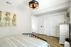 Ein Schlafzimmer mit einem Bett, einem Gemälde von Pferden, einem Kleiderschrank und einer Deckenleuchte.